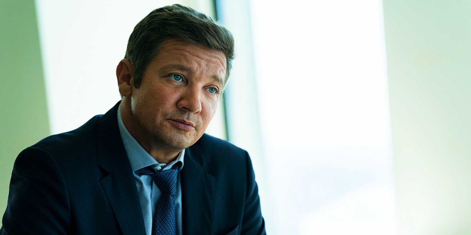 Jeremy Renner as Mike McClusky sitting at table and wearing a suit in Mayor of Kingstown season 2 episode 6