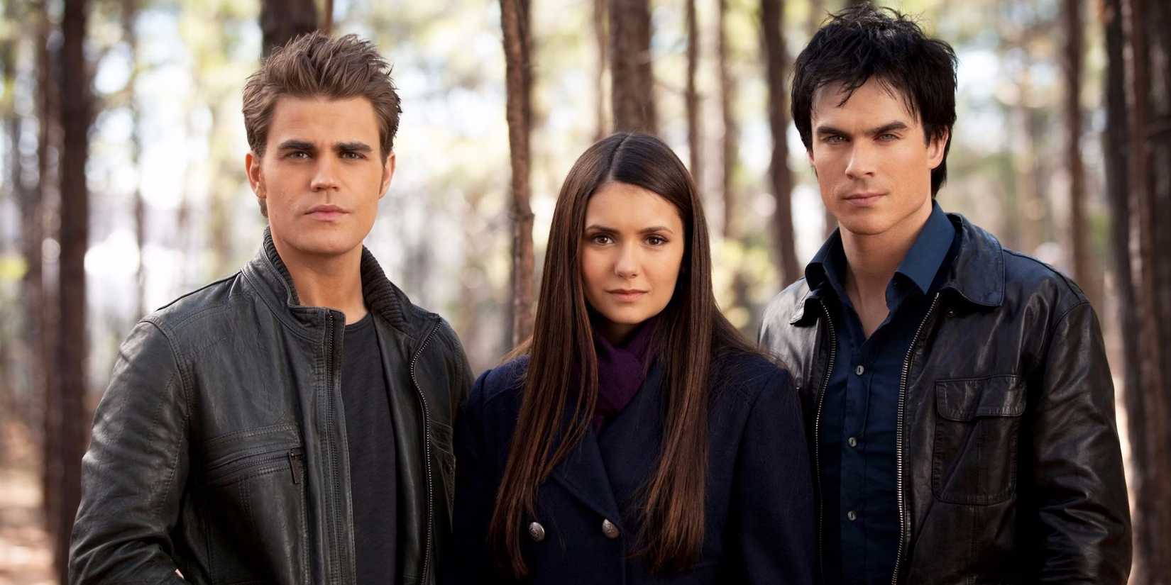 Stefan, Damon, and Elena in the woods staring at the camera in a promotional still in The Vampire Diaries