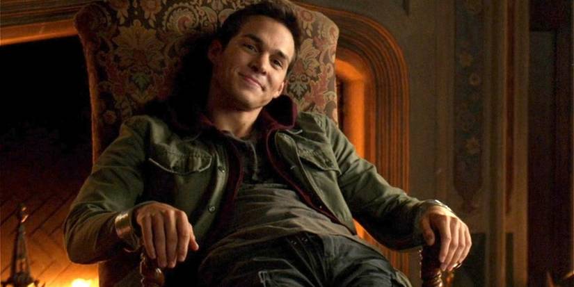 Kai Parker smiles while sitting in a chair in 'The Vampire Diaries'