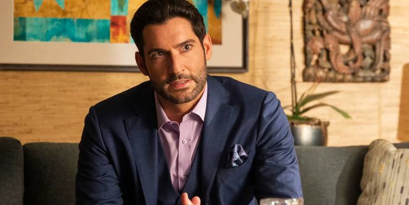 Tom Ellis as the titular protagonist sitting on a couch and wearing a suit in Lucifer