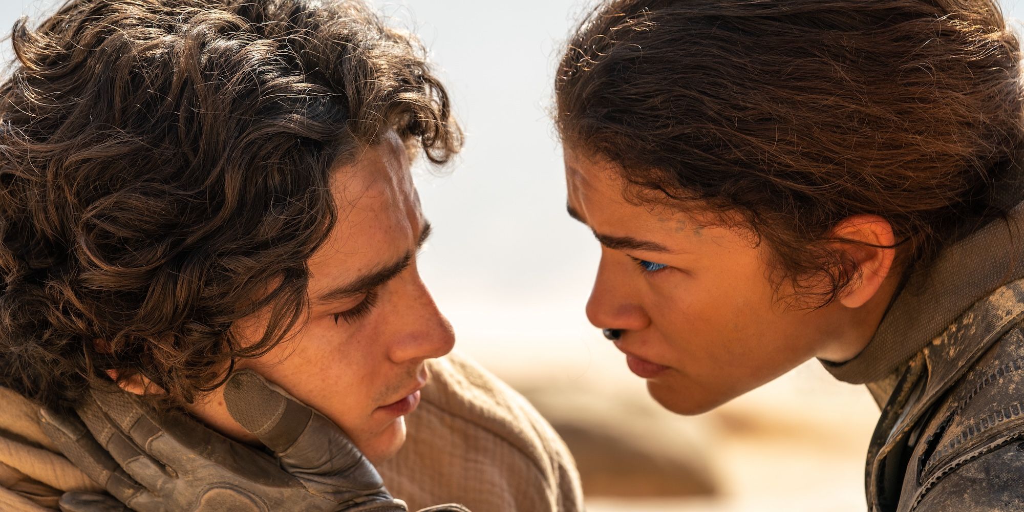 Chani, played by Zendaya, grips Paul's face as they look at each other while in the Arrakis desert in Dune: Part Two.