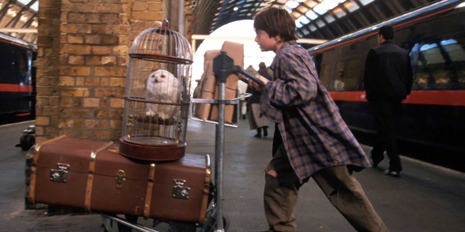 Harry (Daniel Radcliffe) empurra seu malão com Edwiges em sua gaiola na estação Kings Cross em Harry Potter e a Pedra Filosofal