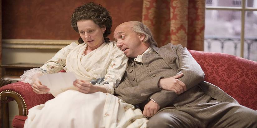 Abigail (Laura Linney) e John Adams (Paul Giamatti) sentados juntos em John Adams.