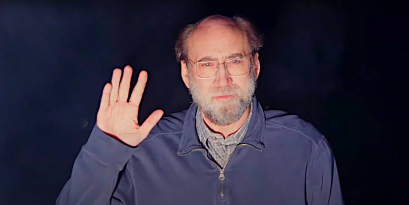 Nicolas Cage standing in bright headlight glare, waving mysteriously, in a scene from Dream Scenario