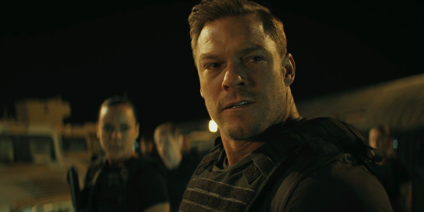 Alan Ritchson as Reacher wearing a bullet proof vest looking troubled