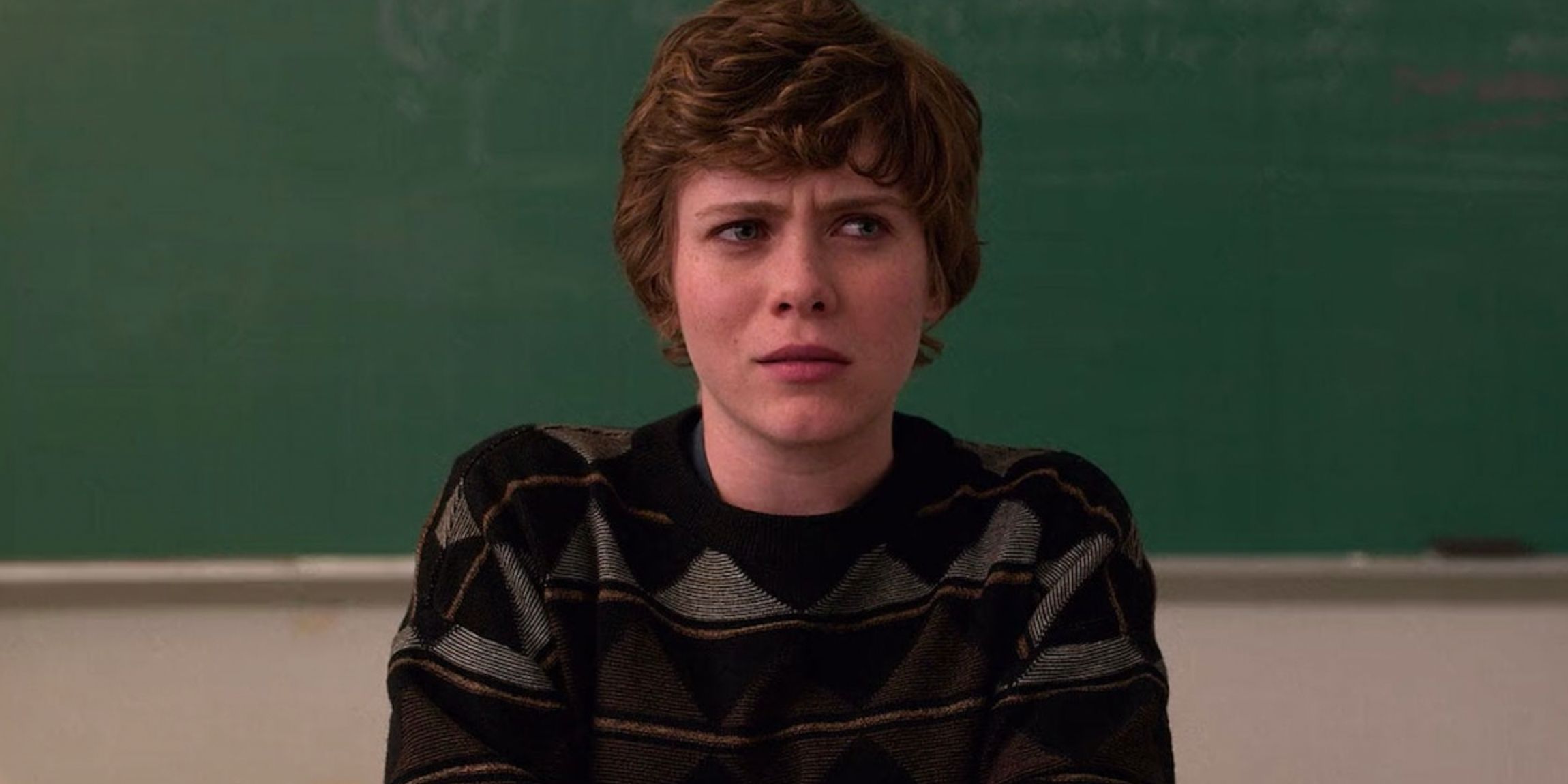 Sophia Lillis as Sydney Novak sitting with a confused and incredulous expression on her face in front of a chalkboard in the Netflix series I Am Not Okay With This