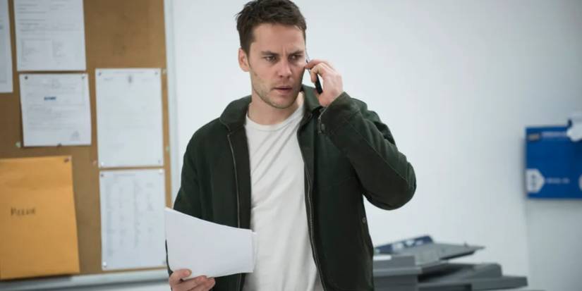 Paul Woodrugh (Taylor Kitsch) en un teléfono celular, sosteniendo papeles y luciendo preocupado en la verdadera temporada de detectives 2