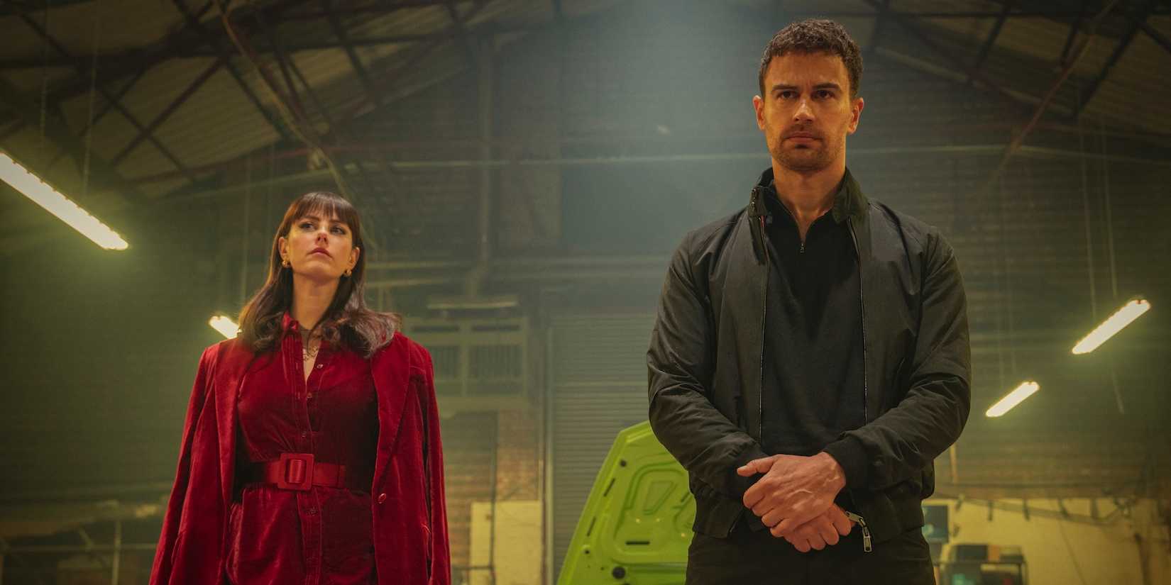 Kaya Scodelario and Theo James stand together in a hangar in The Gentlemen series