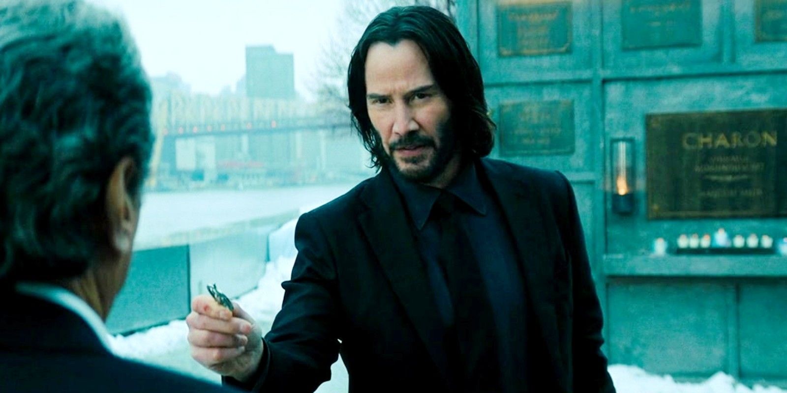 Keanu Reeves as John Wick hands over something to Winston in John Wick 4