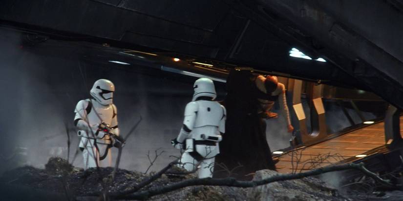 Kylo Ren carrying Rey up the ramp of his ship with stormtroopers looking on.