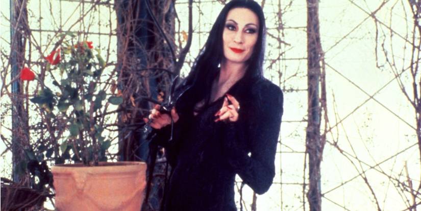 Morticia Addams (Anjelica Huston) in her form-fitting black dress cutting roses in The Addams Family
