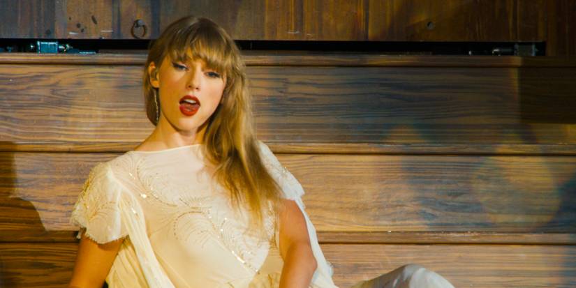 Taylor Swift wears a white dress and sits on wooden steps in Taylor Swift: The Eras Tour (Stream Release).