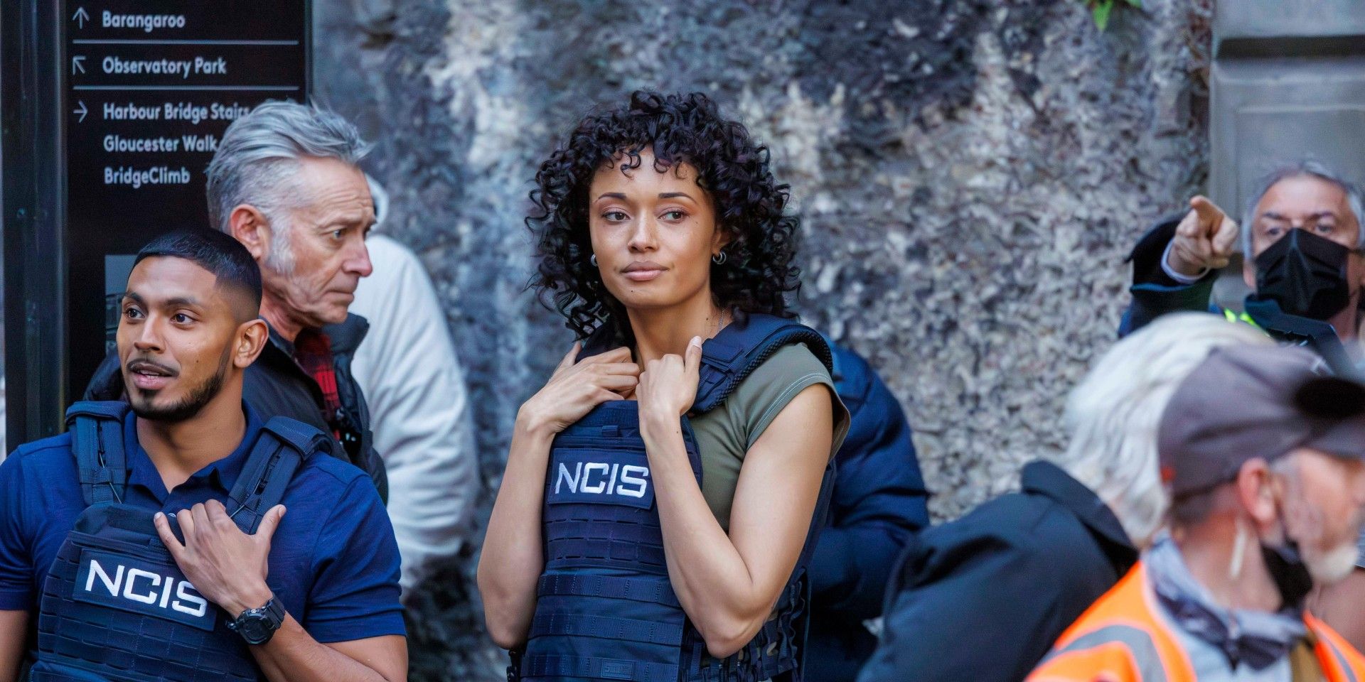 Olivia Swann as Mackey standing in her NCIS vest among a crowd in NCIS Sydney