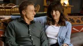 Alan Tudyk as Harry looking at Edi Patterson as Heather in Resident Alien as they sit on the couch