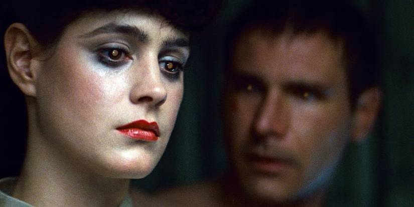 Sean Young as Rachel in Blade Runner stands in the forefront with light inclusions in her eyes. Harrison Ford as Deckard stands behind her in shadow.