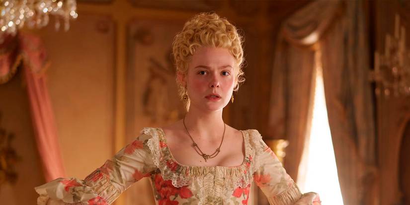 Elle Fanning as Catherine standing with her hands on her hips in full court finery while looking at someone in confusion in The Great