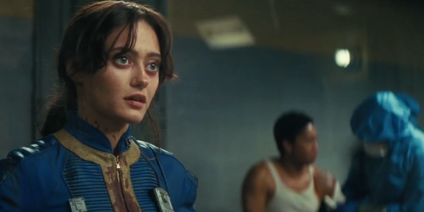 Ella Purnell como Lucy com um uniforme ensanguentado enquanto alguém é tratado atrás dela em Fallout