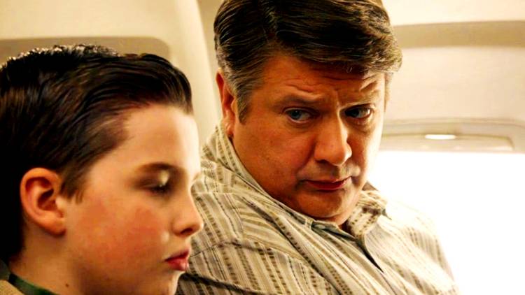 Sheldon and George sitting on a plane, with George looking at Sheldon, in Young Sheldon