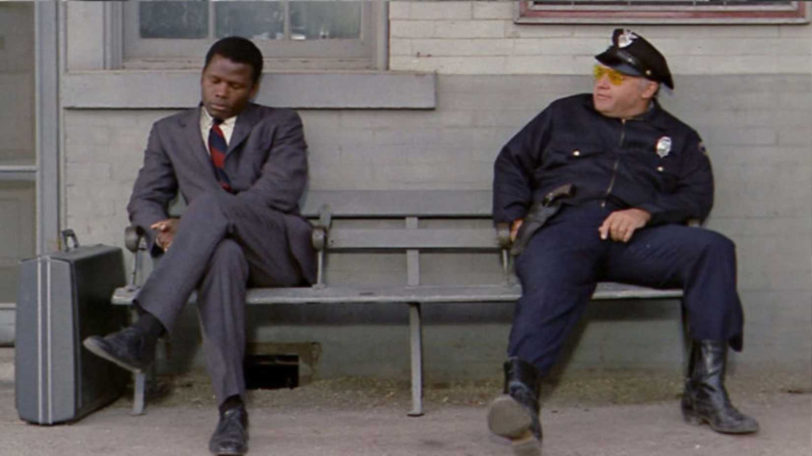 Sidney Poitier and Rod Stieger sit on a bench in In the Heat of the Night