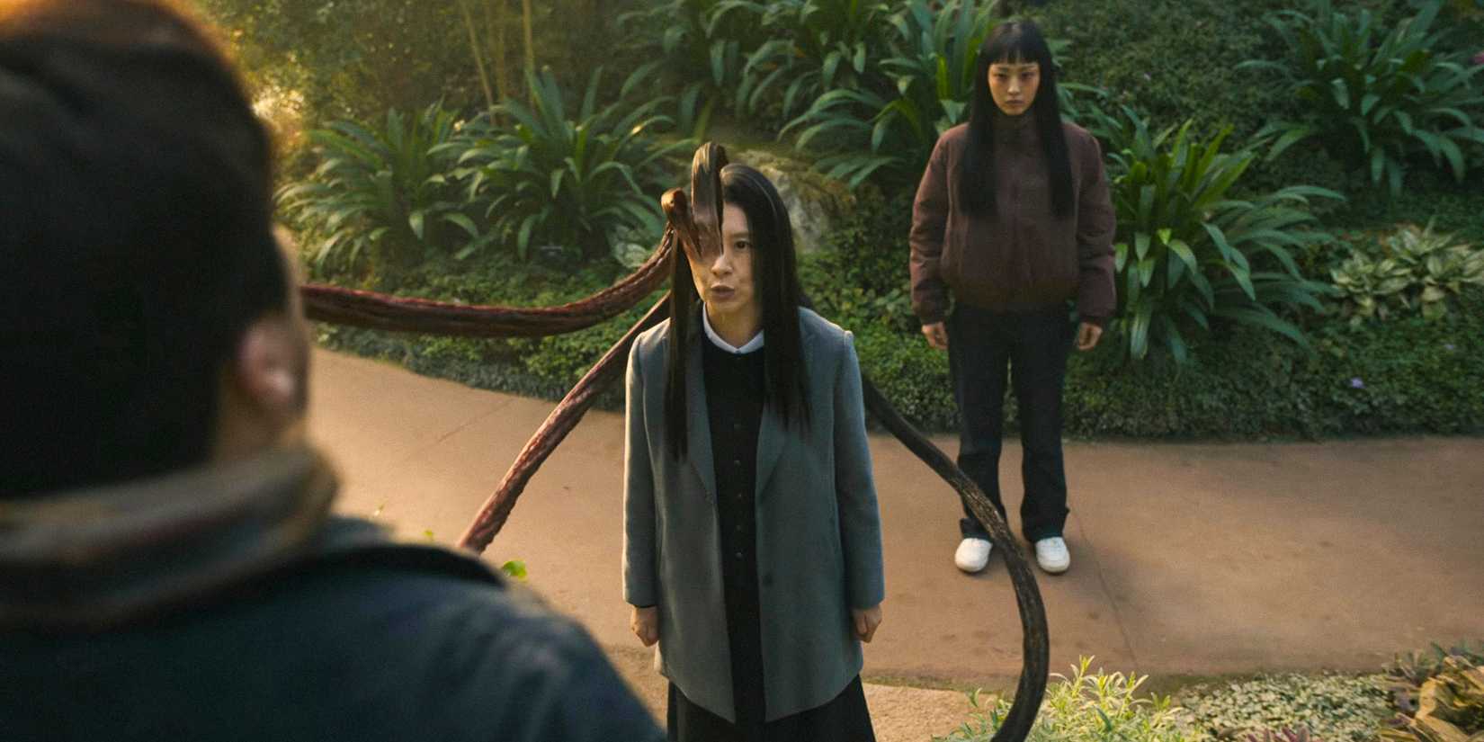 Seol Kyung Hee como um parasita segurando um homem pelo pescoço, com Jeong Su-in atrás dela em Parasyte: The Grey temporada 1