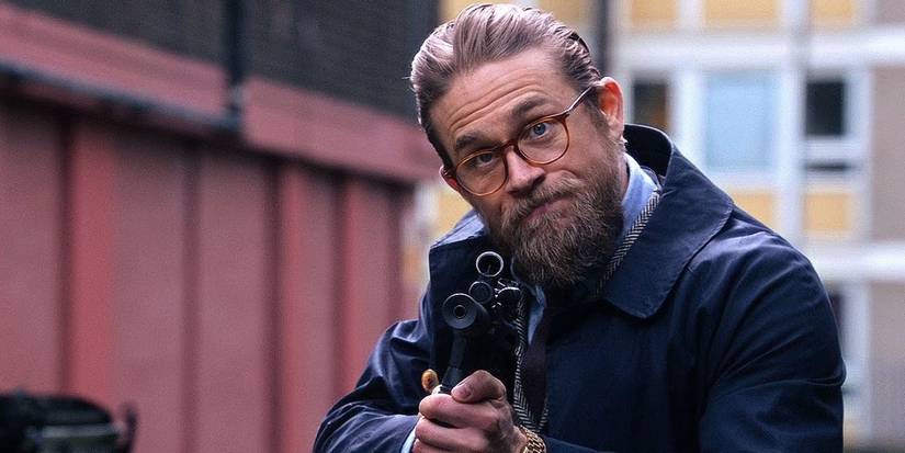 Raymond (Charlie Hunnam) pointing a gun and smiling in The Gentlemen.