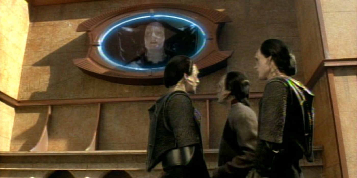 Three Cardassians stand on a city street with an oval screen in the background