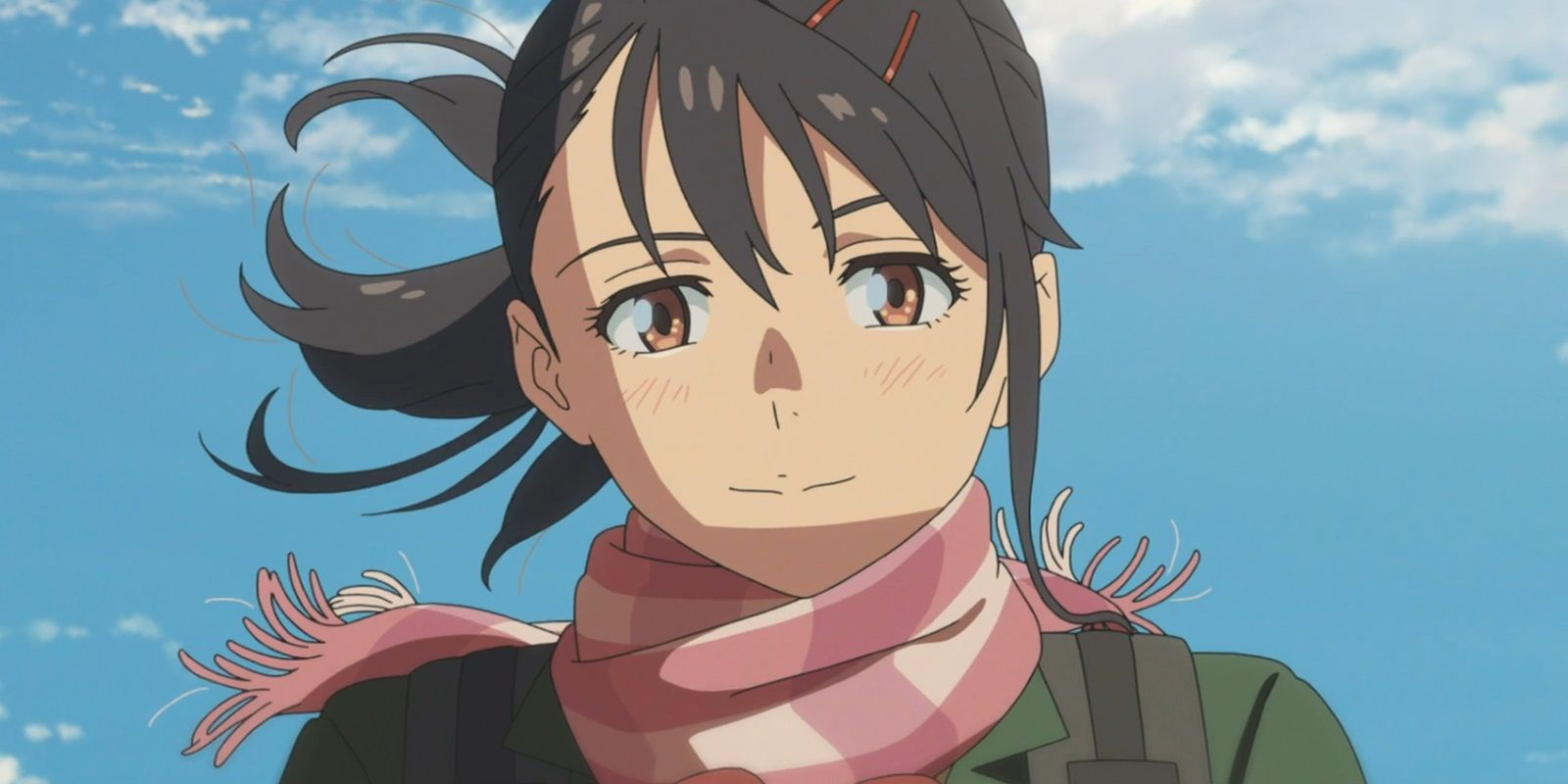 Suzume di adegan terakhir film, tersenyum hangat sementara rambut dan syalnya tertiup angin di hari yang cerah.