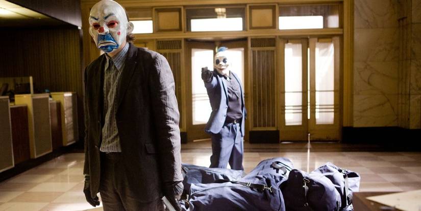 A masked clown holds another masked clown at gunpoint in The Dark Knight (2008) opening bank heist