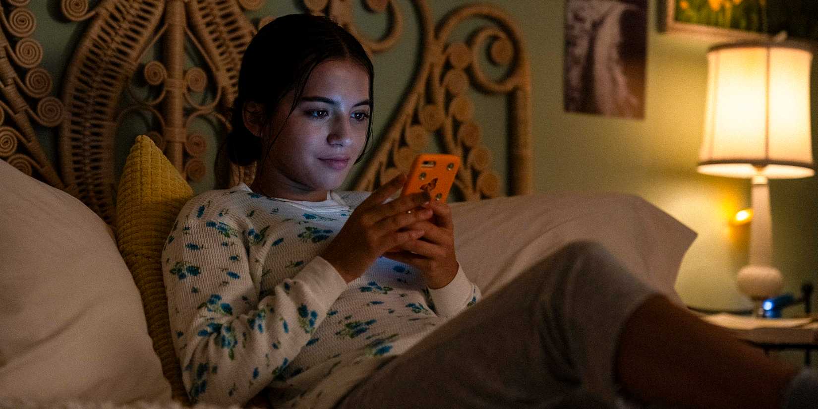 Aza Holmes in her bedroom looking at her phone, smiling brightly in Turtles All The Way Down.