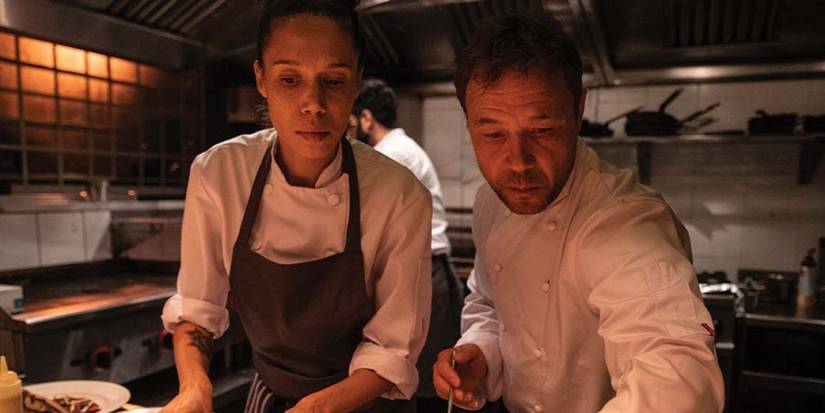Stephen Graham als Andy und Vinette Robinson als Carly servieren gemeinsam Essen in einer Küche in Boiling Point. 