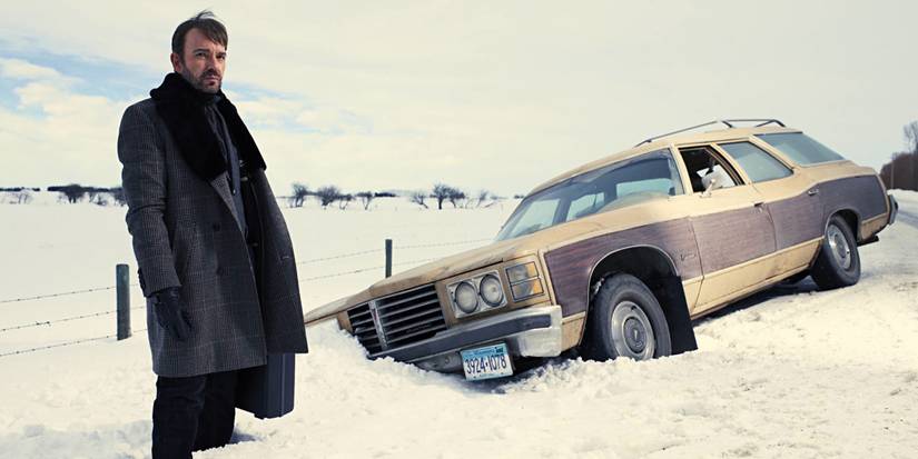 Billy Bob Thorton standing next to a car wrecked in a snow bank in Fargo season 1