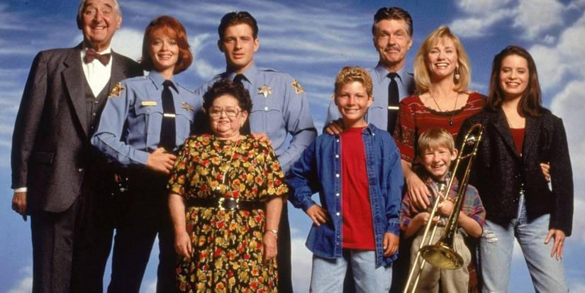 The whole cast of Picket Fences smiling in front of a sky background