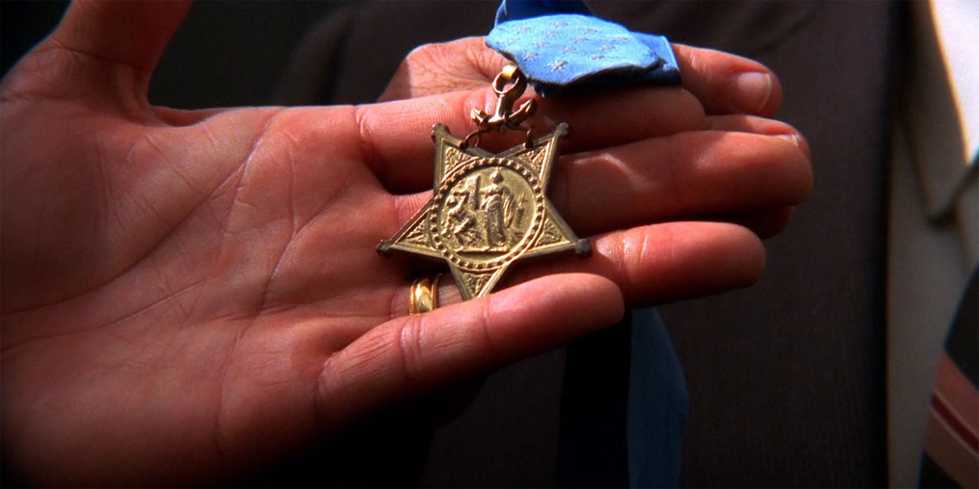 A close up of a hand holding a Medal of Honor in NCIS