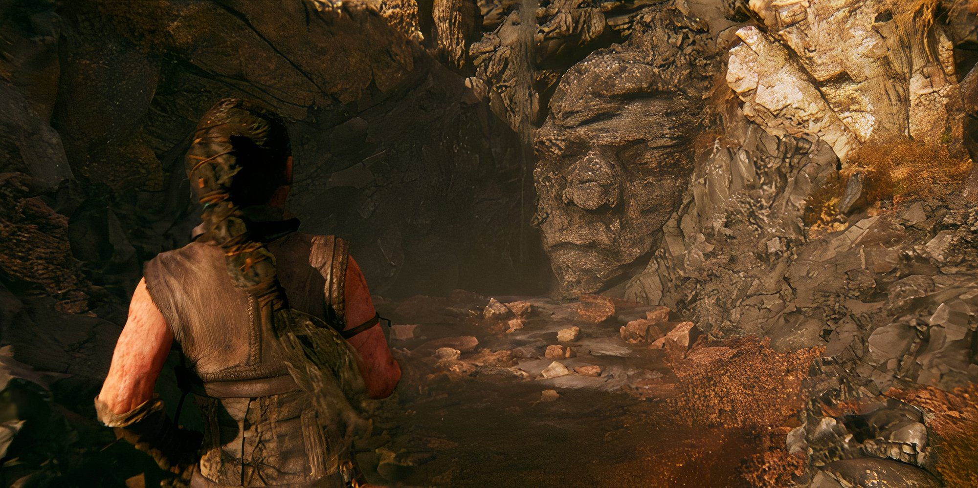 Senua se aproxima de um rosto escondido esculpido nas rochas em Hellblade 2