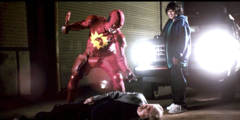 Rainn Wilson como Crimson Bolt em pé sobre um criminoso em Super