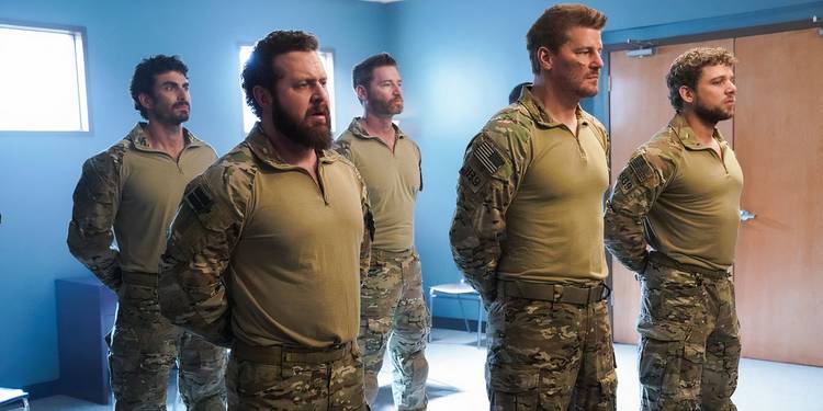 The main cast of SEAL Team standing at attention in a barracks.