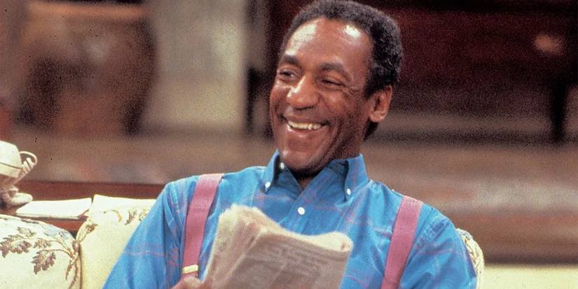 Bill Cosby as Cliff Huxtable laughing and holding a newspaper in The Cosby Show