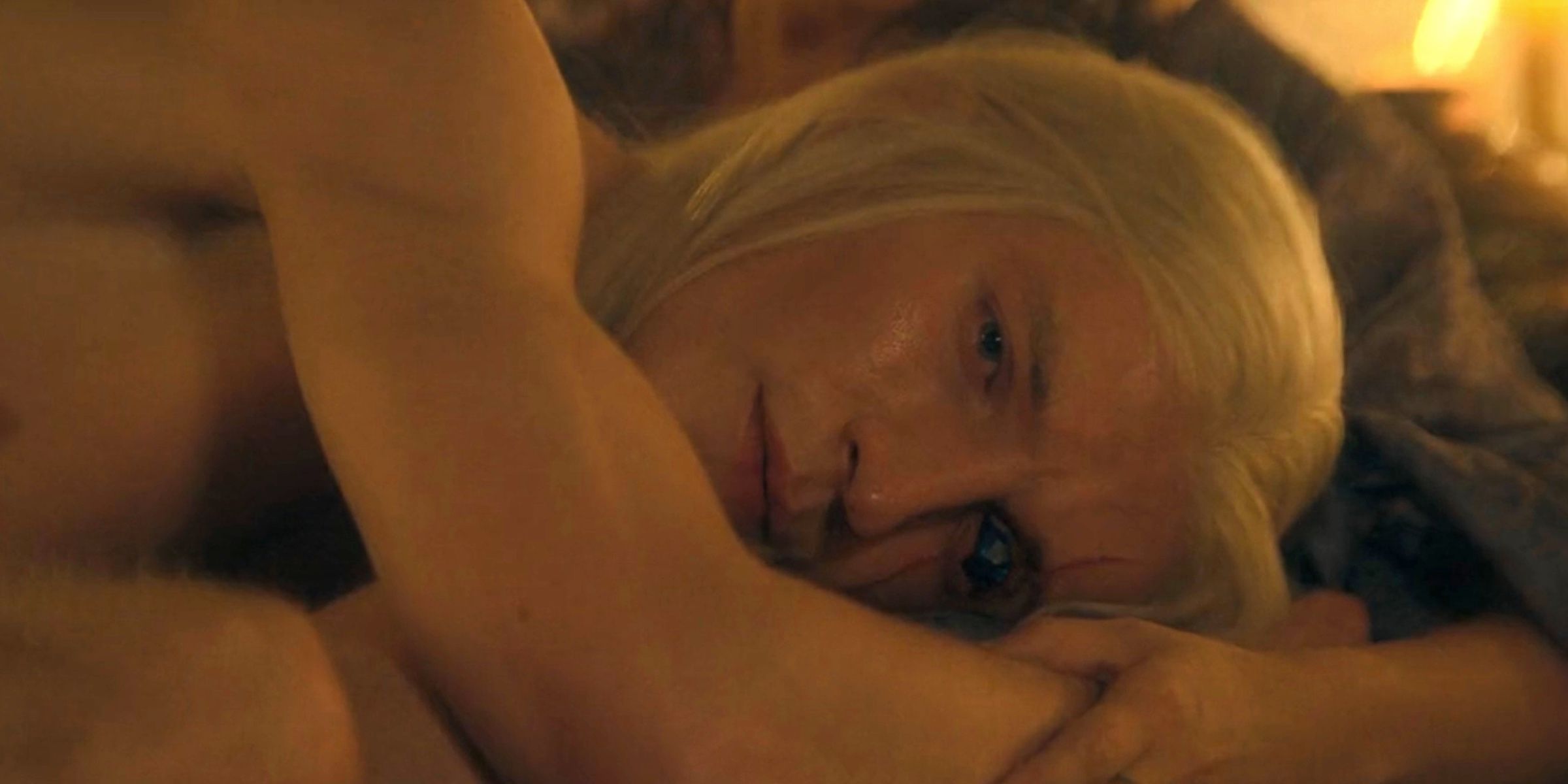 Aemond Targaryen lying down on his side with Sylvi holding him in House of the Dragon season 2 episode 2