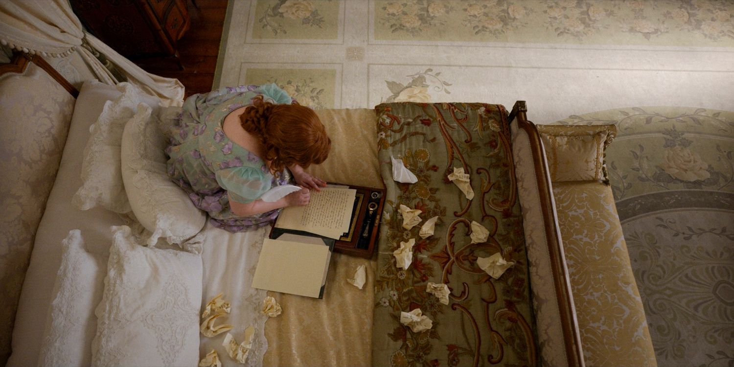 Aerial shot of Penelope (Nicola Coughlan) sitting on her bed writing, surrounded by many crumpled pieces of paper in Bridgerton season 3 episode 6