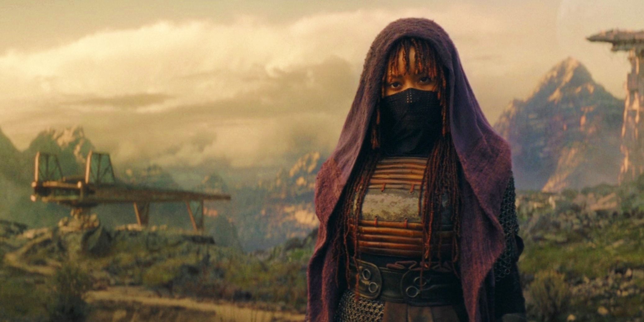 Mae standing on Ueda in The Acolyte with her mask and hood up and a ship and mountain in the background