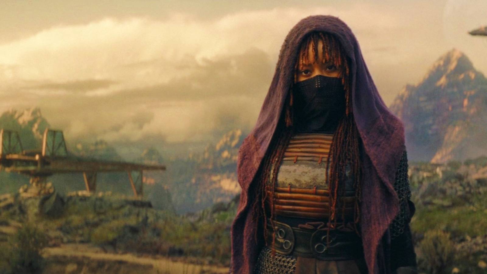 Mae standing on Ueda in The Acolyte with her mask and hood up and a ship and mountain in the background