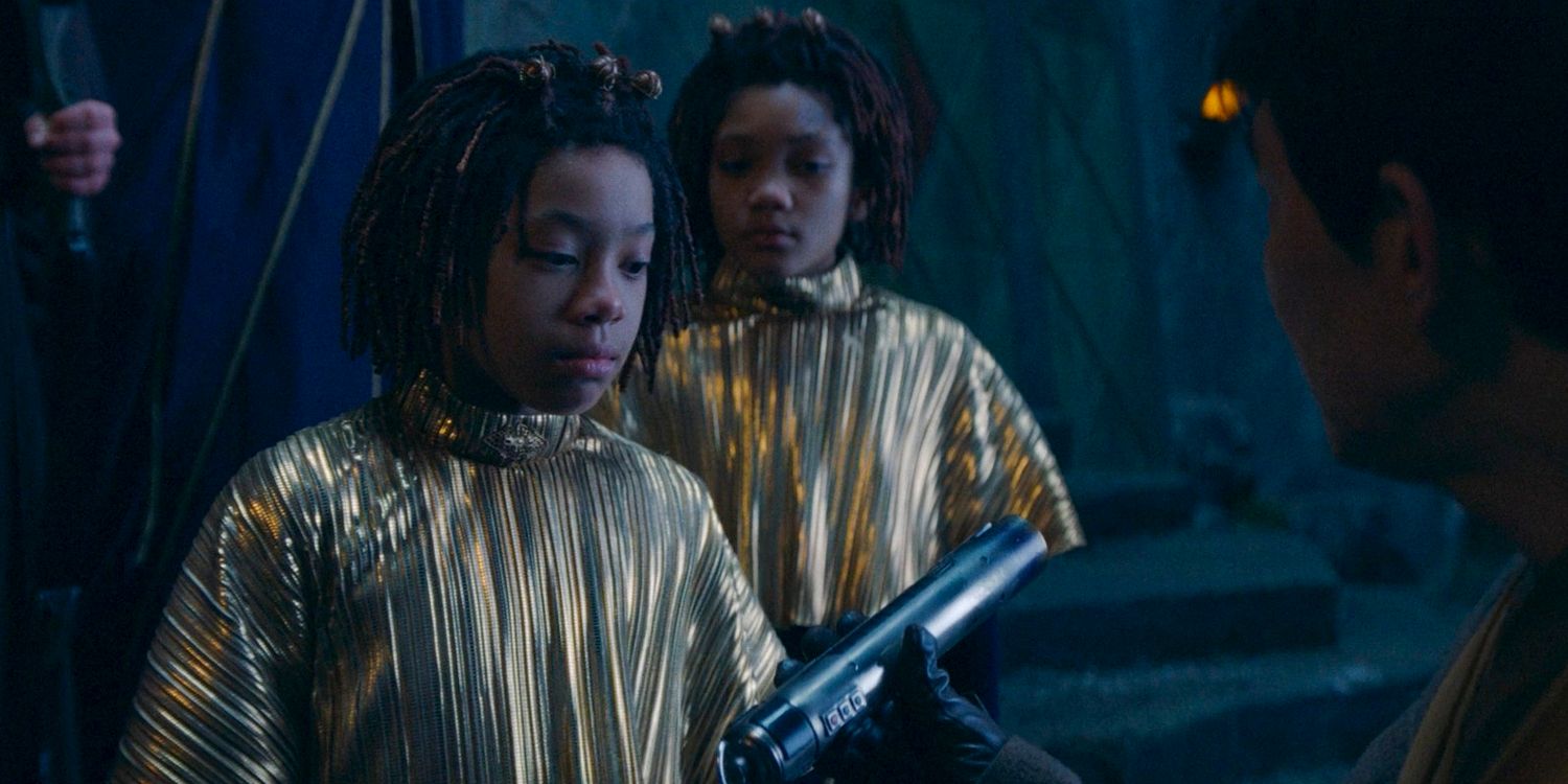 Younger Master Sol showing the hilt of a lightsaber to Little Osha (Lauren Brady) while Little Mae (Leah Brady) watches in The Acolyte season 1 episode 3