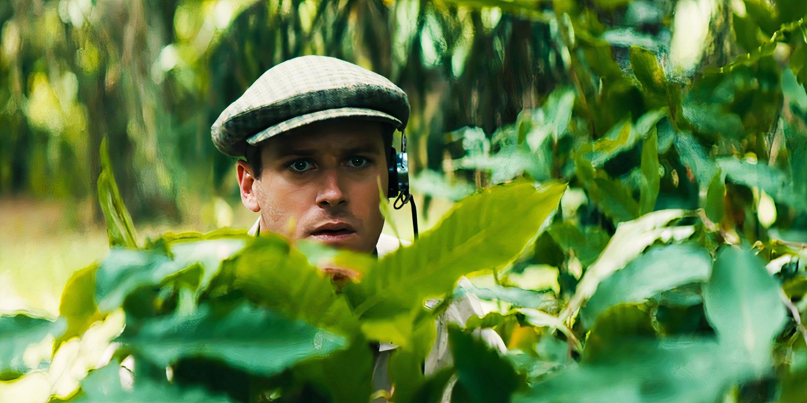 Armie Hammer as Illya Kuryakin in The Man From U.N.C.L.E peering out from behind some leaves