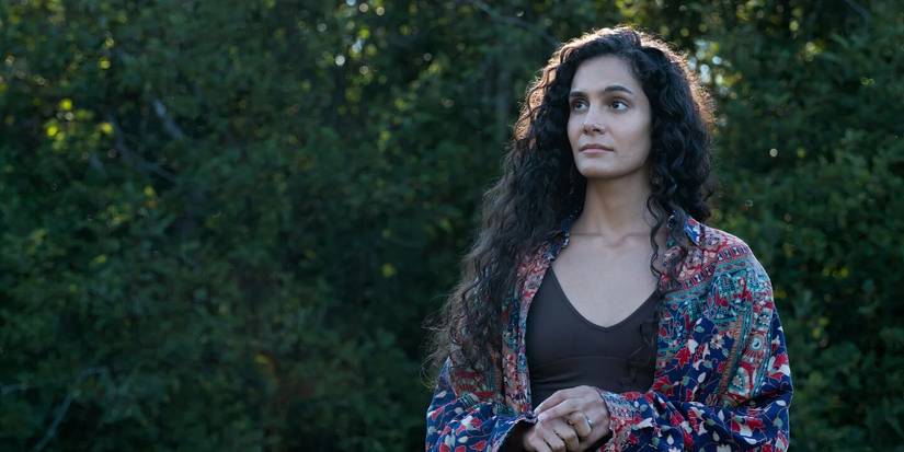 Fatima looks on while standing with her hands clasped near the woods in From