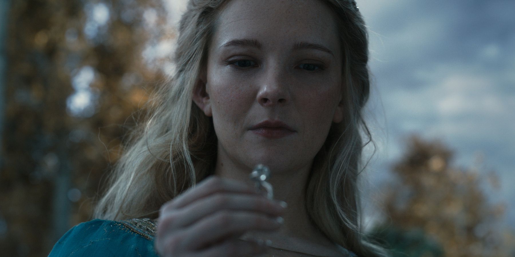 Morfydd Clark as Galadriel examining a ring underneath an overcast sky in The Lord of the Rings The Rings of Power season 2