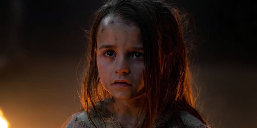 Isla Gie looks up with fear with her face covered in soot near a fire in Foundation