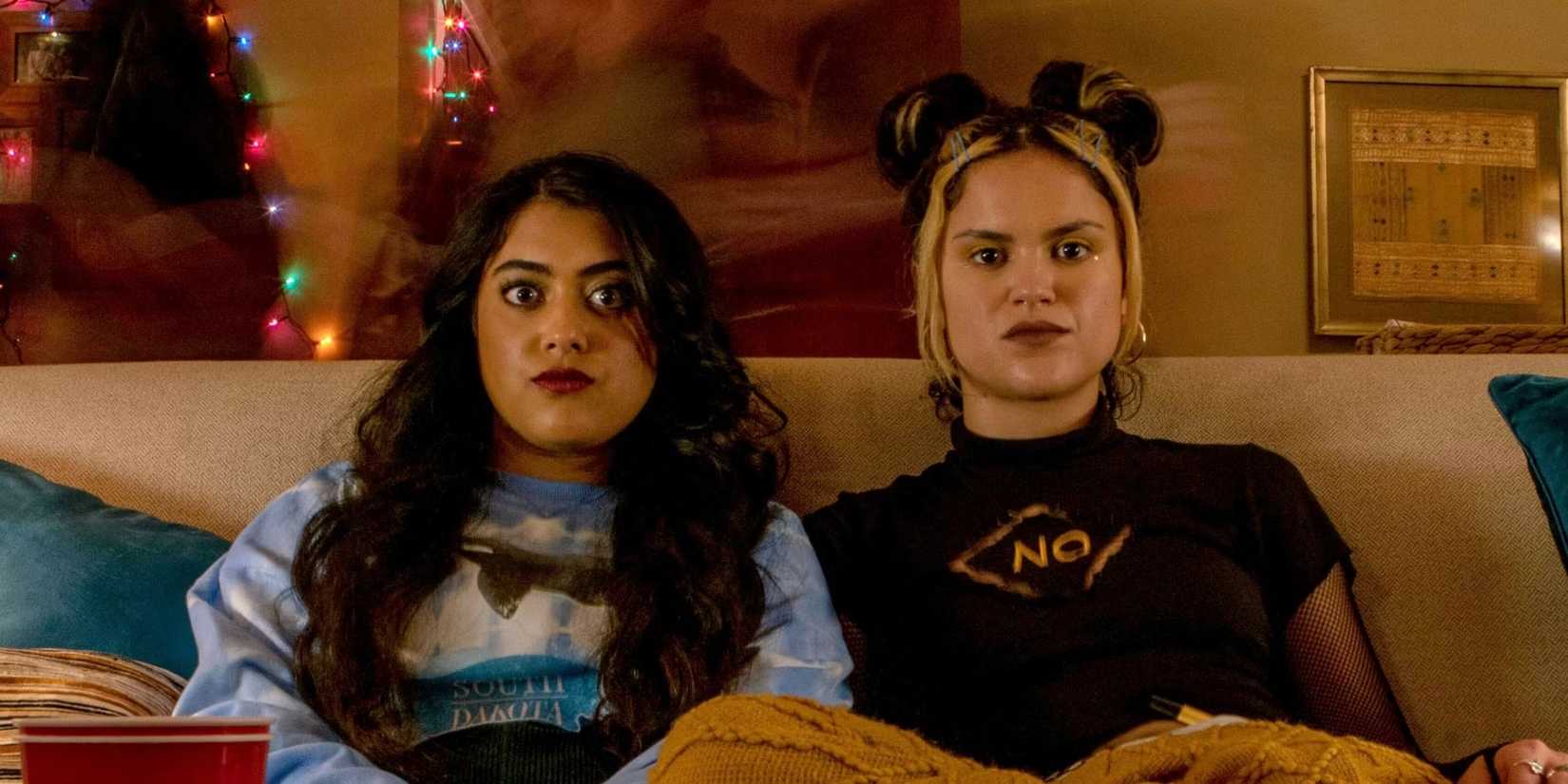 Kuhoo Verma como Sunny e Victoria Moroles como Lupe sentadas juntas no sofá em Plan B.
