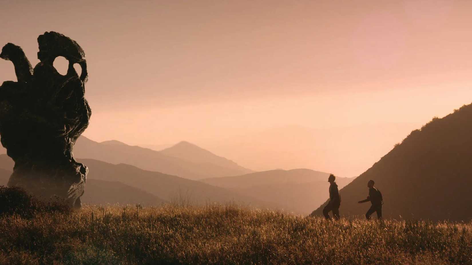 Two men walking towards a giant monolith in The Endless