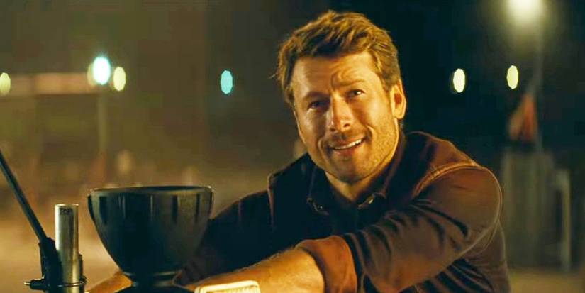 Glen Powell (Tyler Owens) smiling while leaning against his truck in Twisters
