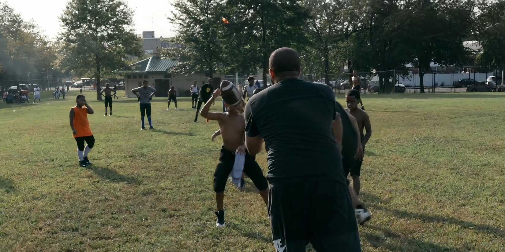 Coach looking at boy holding football in We Are The Brooklyn Saints on Netflix